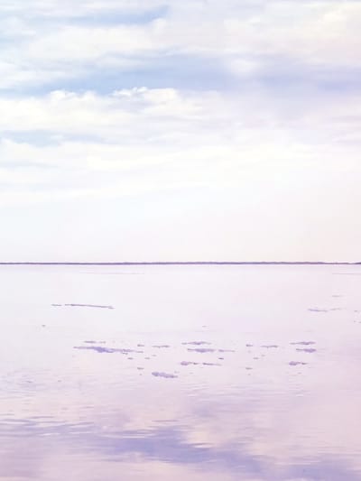 Person stands on reflective ground, looking at blue and pink sky and clouds.